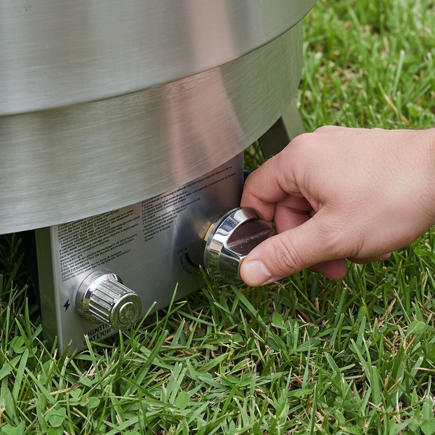 Hand adjusting a knob on a stainless steel grill in grass - Slinky Stove